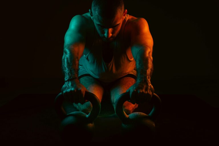A strong man intensely working out with kettlebells in a dark gym setting.