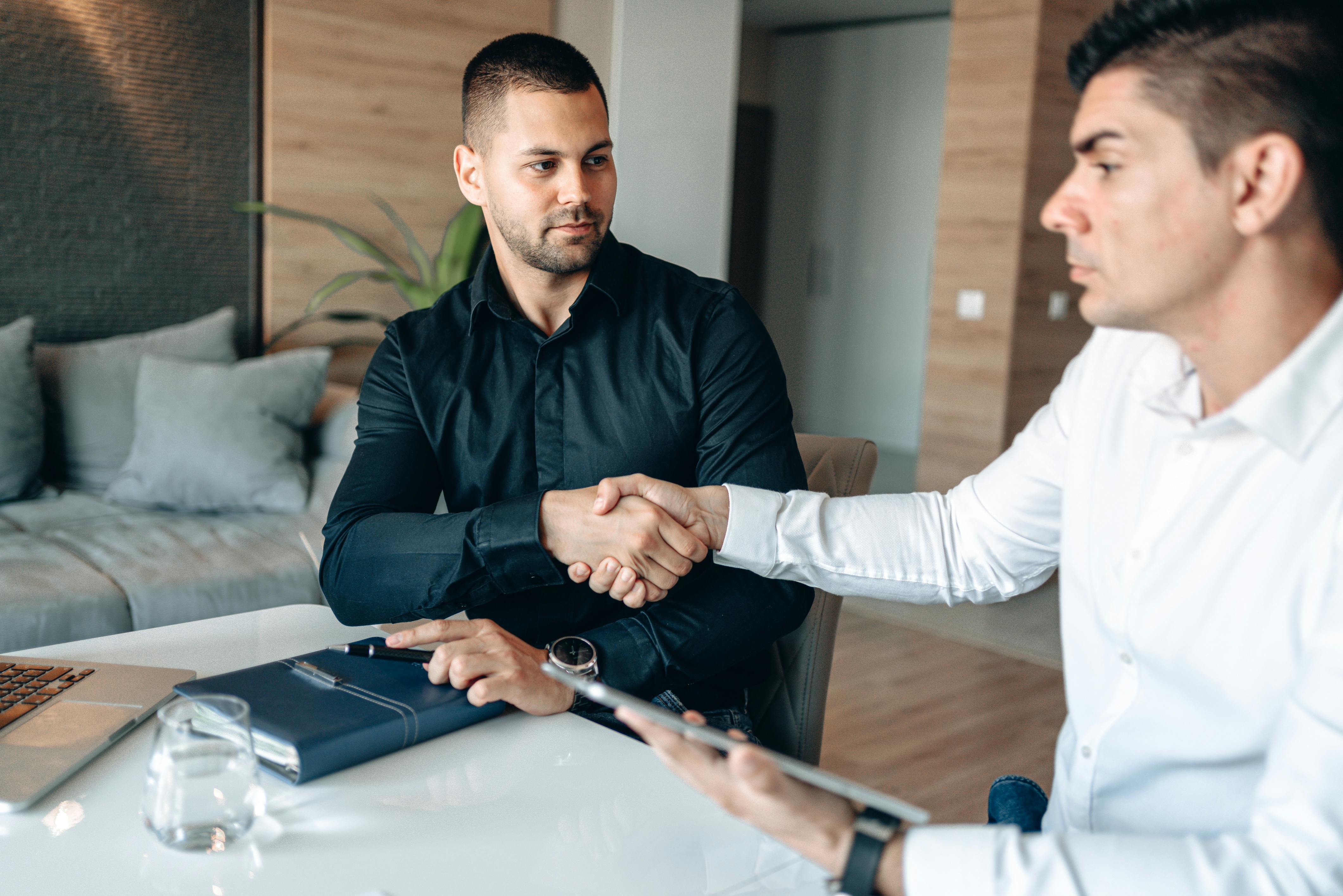Two businessmen shaking hands over a deal in a modern office environment.